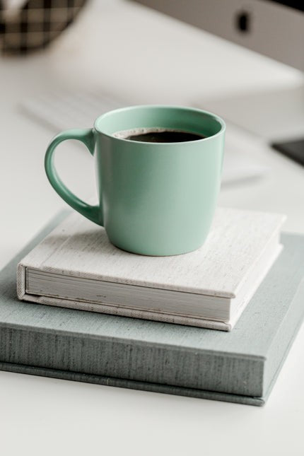 Green mug with coffee on a stack of books on a light surface